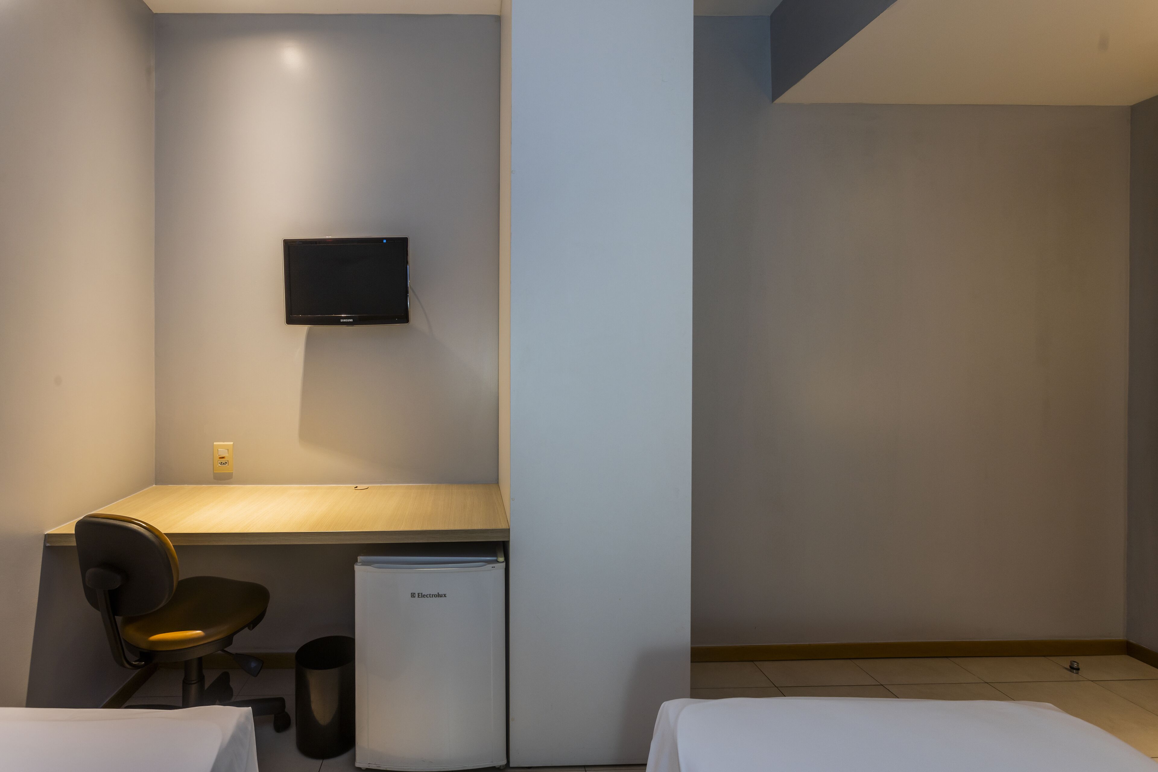 Habitación de hotel con cama, escritorio con silla, televisión montada en la pared y un refrigerador pequeño.