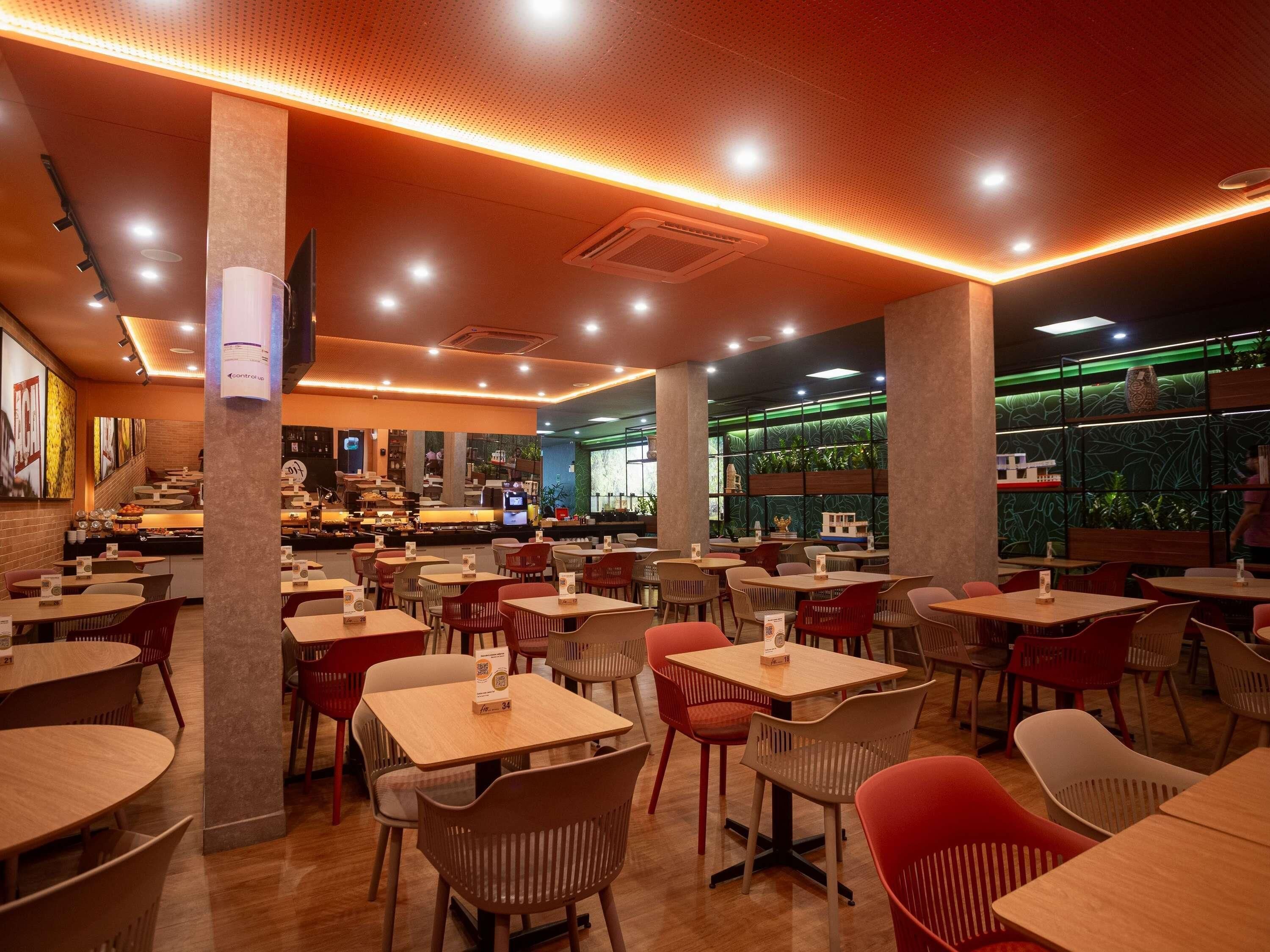 A restaurant interior with multiple tables and chairs, a bar area, and a green wall with plants.
