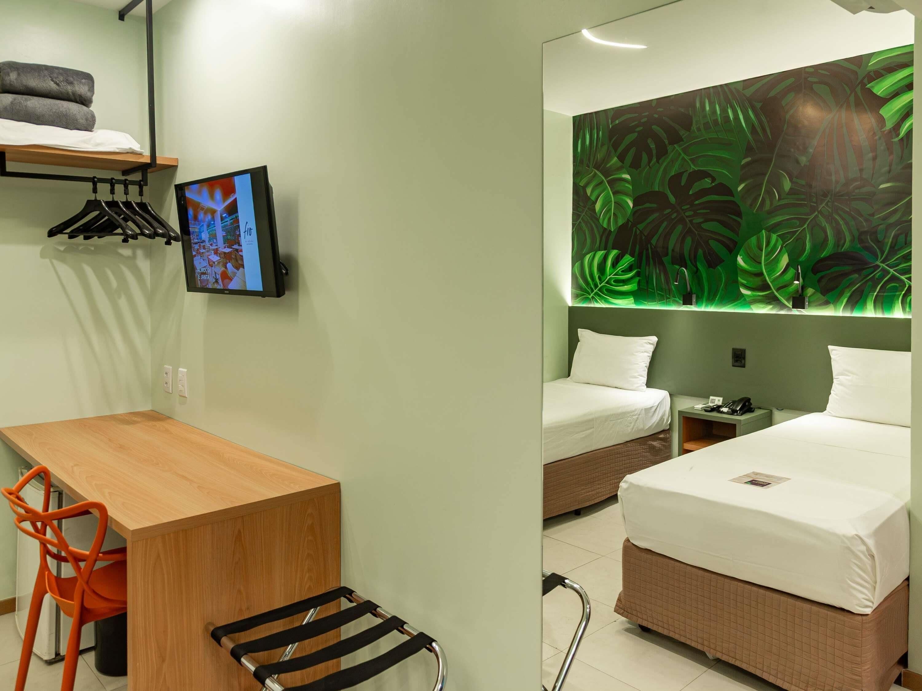 Een hotelkamer met een bed, een bureau, een stoel, een televisie en een muur met een bladmotief.