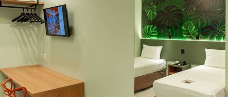 Een hotelkamer met een bed, een bureau, een stoel, een televisie en een muur met een bladmotief.
