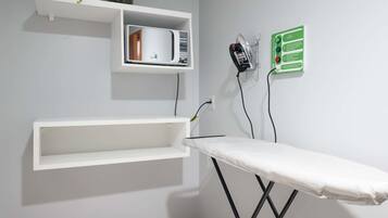 Um quarto com uma tábua de passar branca, uma prateleira com micro-ondas e um letreiro verde na parede.