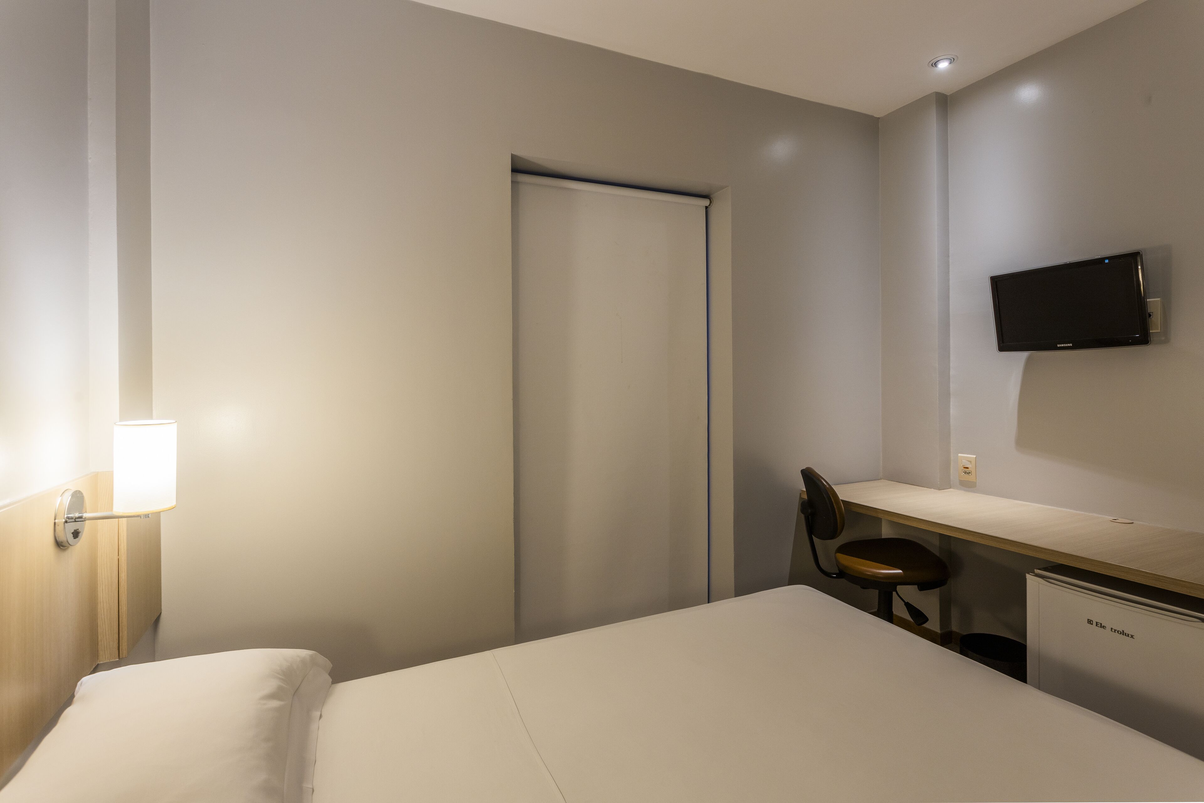 Una camera d'albergo con un letto, una scrivania, una sedia, una TV e un minibar.
