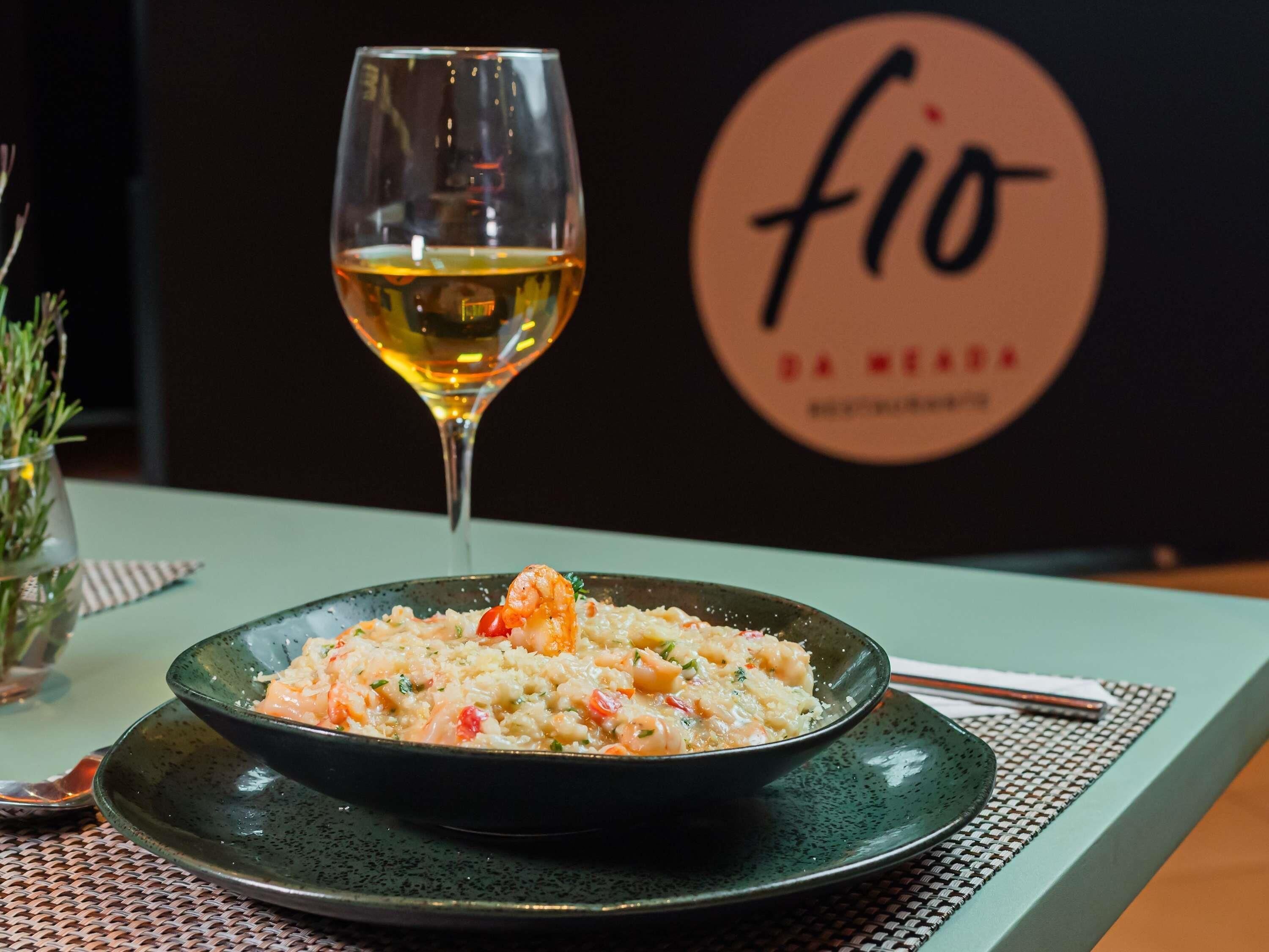 Een schaal zeevruchtenrisotto op een bord met een glas witte wijn op een tafel.