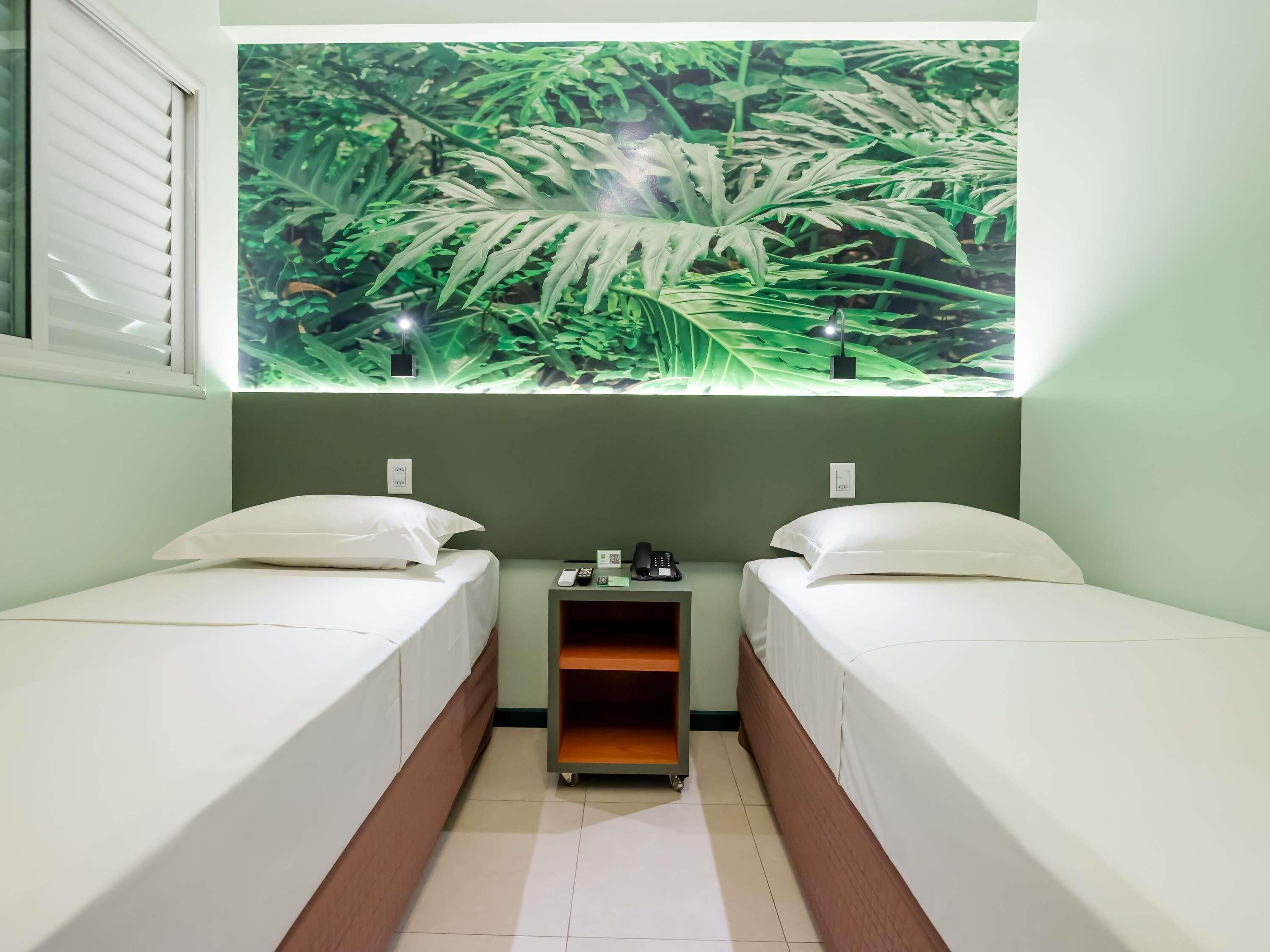 A small, clean room with two single beds, a nightstand with a phone and a lamp, and a wall-mounted shelf.