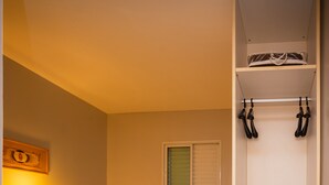 Una habitación de hotel con dos camas, un armario, una mesita de noche con lámpara y una ventana con persianas.