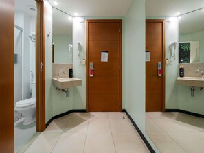 Un baño de hotel con lavamanos, espejo y puerta con un cartel.