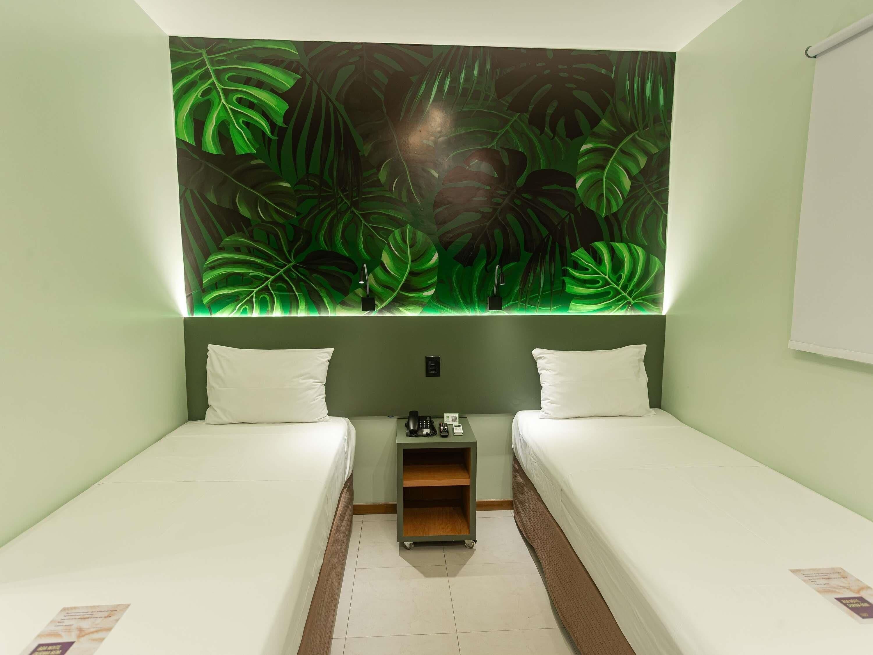 A room with two single beds, a small bedside table with a lamp, and a wall-mounted light fixture.