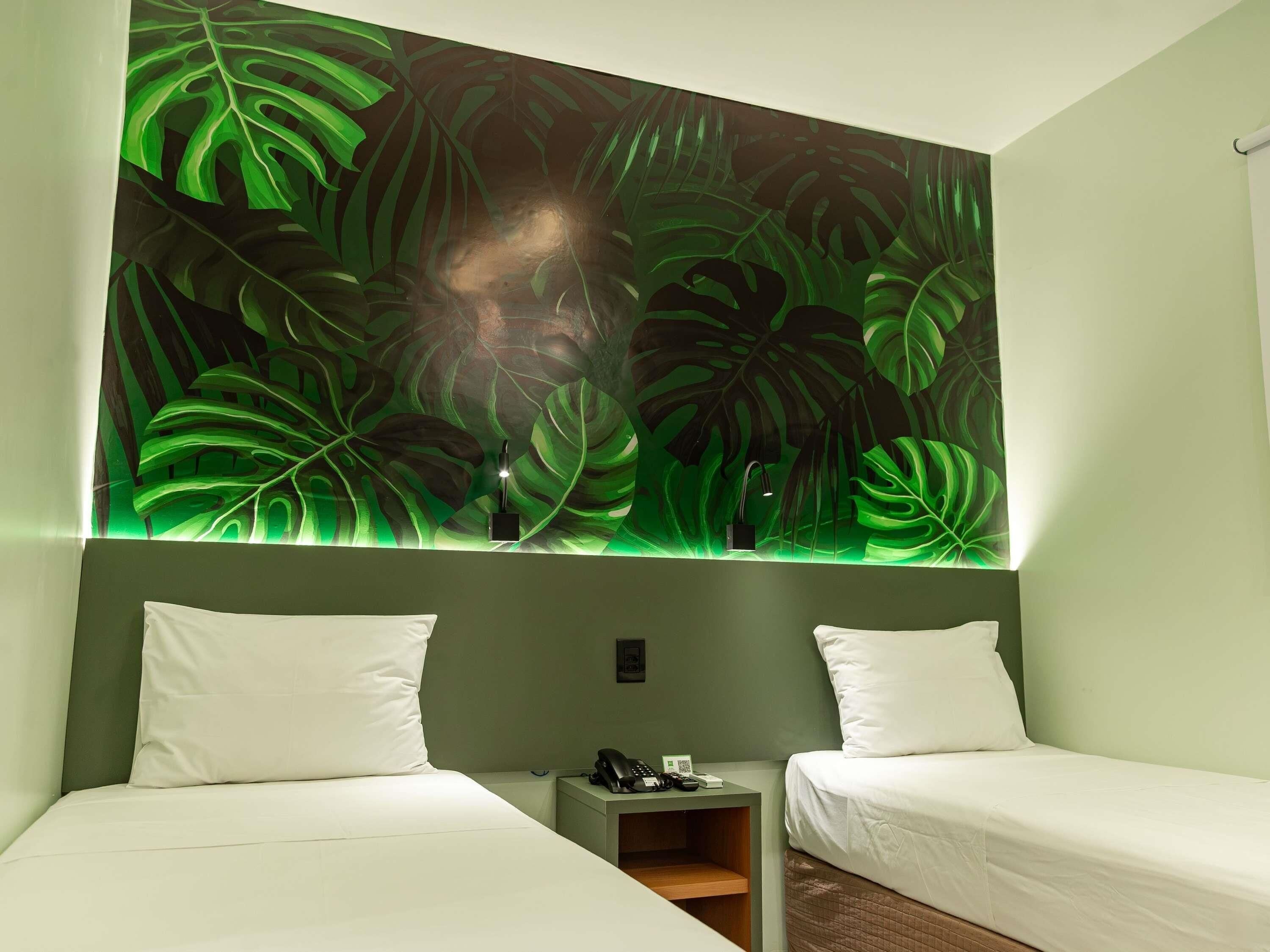 Une chambre avec deux lits, une table de chevet et un mur orné d’un grand motif de feuilles tropicales.