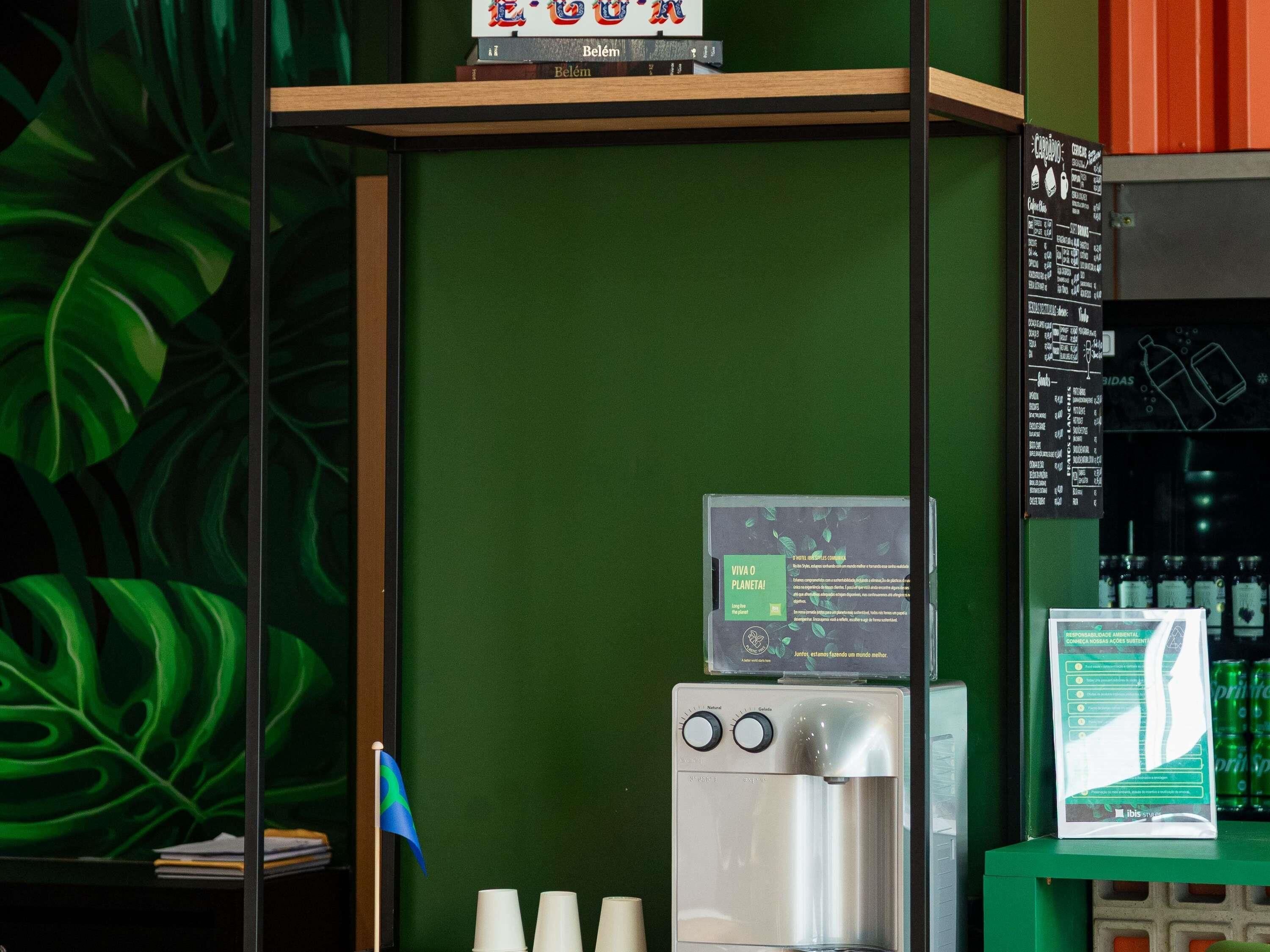 A green wall with a water dispenser, a menu board, and a shelf with books.