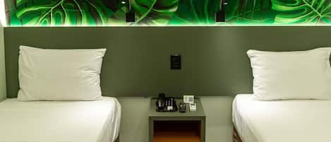 Een hotelkamer met twee bedden, een kleine tafel met telefoon en lamp, en een wand met een bladerenpatroon.