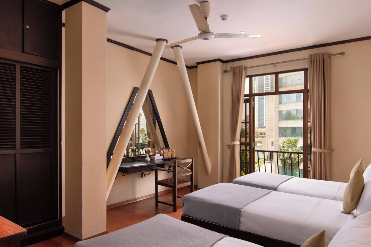 A hotel room with two beds, a desk, a chair, a ceiling fan, and a window with curtains.