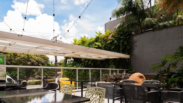 Een terras buiten met tafels en stoelen, omringd door groen en een witte luifel.