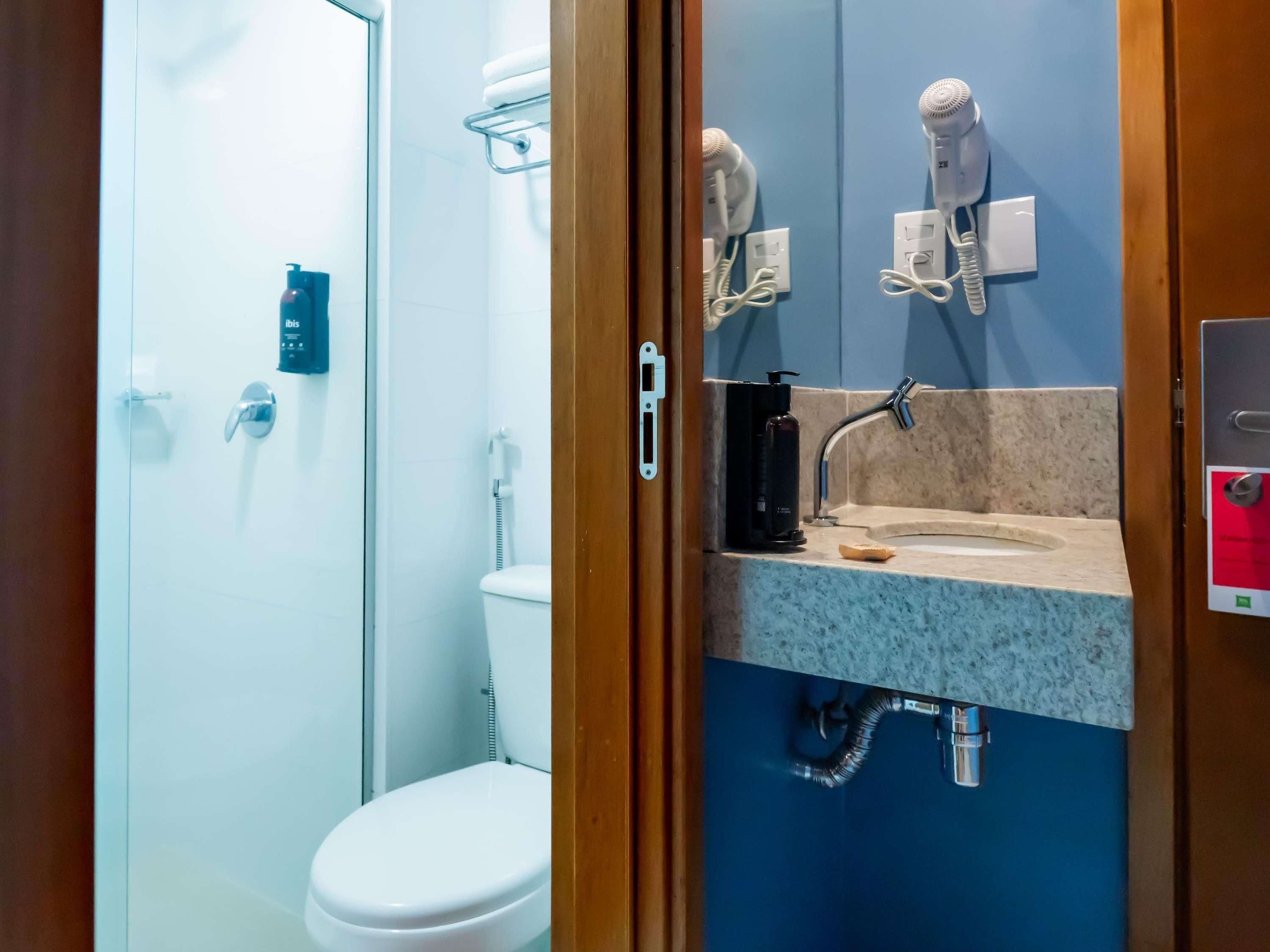 Un baño con inodoro, lavamanos con dispensador de jabón y secador de pelo montado en la pared.