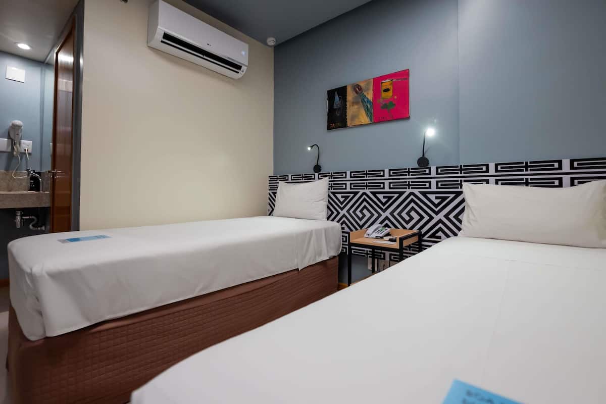 Habitación de hotel con dos camas individuales, aire acondicionado de pared, mesita de noche con teléfono y un cuadro en la pared.