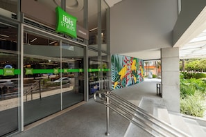A modern building with a green 'ibis styles' sign, glass storefront, and a colorful mural. - Ibis Styles Belém Hangar (Belém)