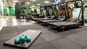 Een sportschool met loopbanden, krachtapparaten en een mat met groene fitnessballen.