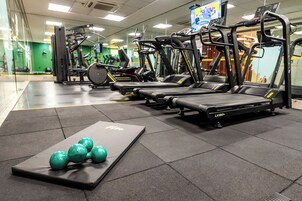 Academia com esteiras, máquinas de musculação e um tapete com bolas de ginástica verdes.