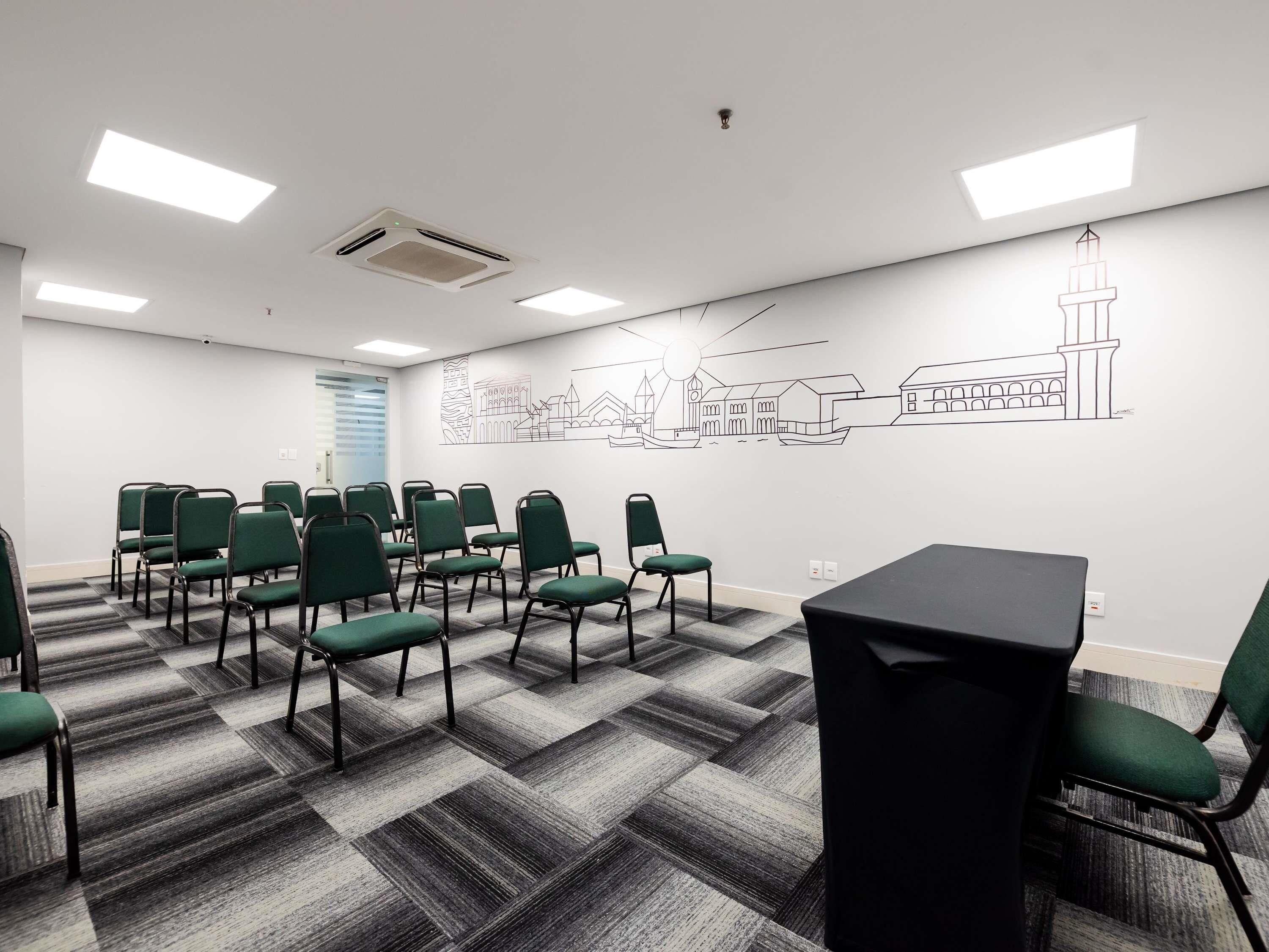 Un salón de conferencias con sillas verdes, una mesa negra y un mural en la pared.