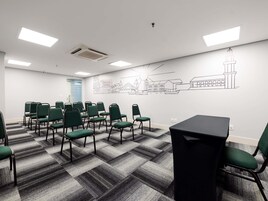 Uma sala de conferência com cadeiras verdes, uma mesa preta e um mural na parede.