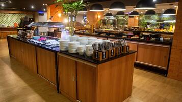 Disposição de buffet com diversas estações de serviço, variedade de alimentos e uma planta central.