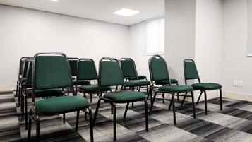 A conference room with green chairs, a checkered carpet, white walls, and a window.