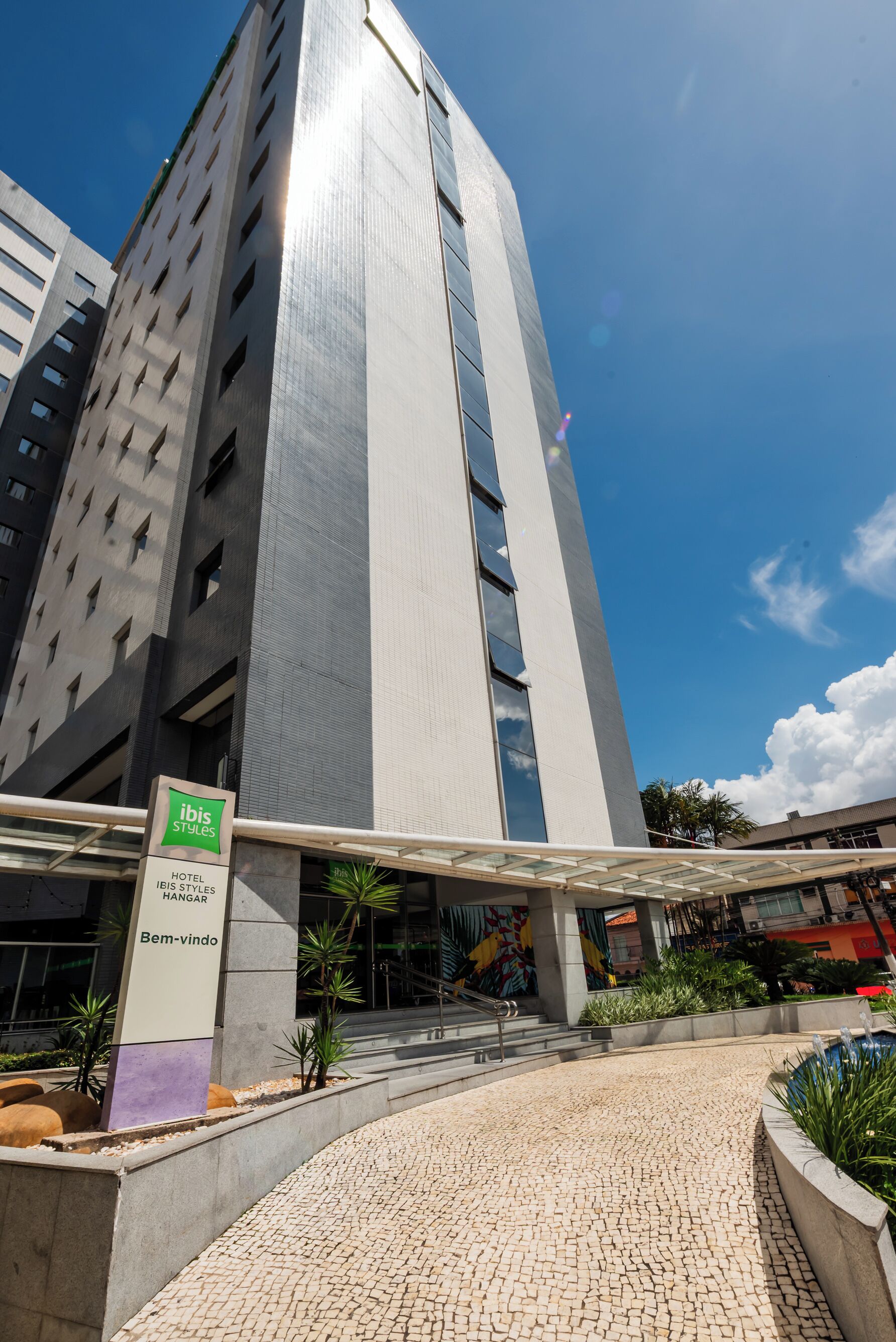 A modern hotel entrance with a prominent sign for ibis Styles Hotel Hangar.