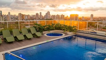 Piscina en la azotea con sillones de descanso y vistas a la ciudad al atardecer.