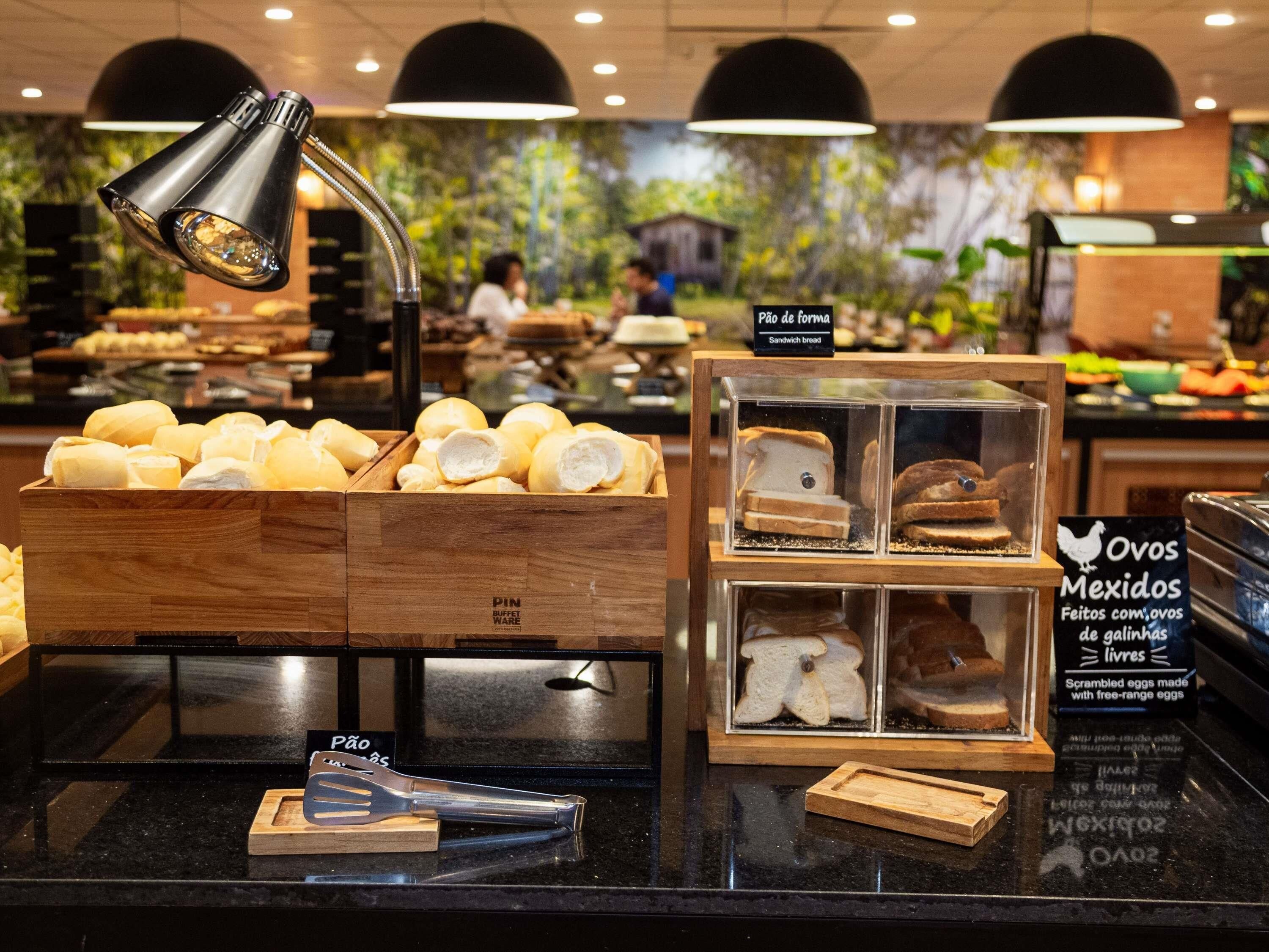Zona de bufé con pan y sándwiches, un cartel que dice 'Pão de forma' (pan para sándwiches) y una bandeja con 'Ovos Mexidos' (huevos revueltos de gallinas criadas en libertad).