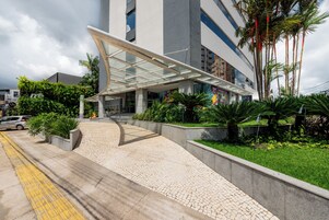 Um edifício moderno com entrada coberta, caminhos pavimentados e áreas verdes ao redor.