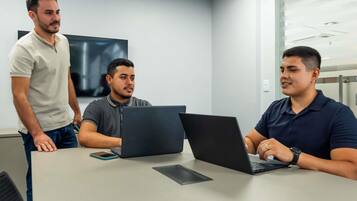 A meeting room with three individuals, two laptops, and a smartphone on a table.
