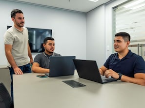 Une salle de réunion où se trouvent trois personnes, deux ordinateurs portables et un téléphone intelligent, le tout posé sur une table.