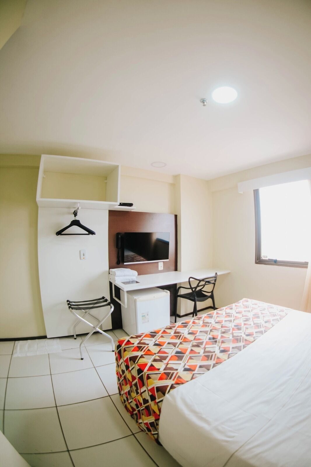 A compact hotel room with a bed, a desk, a chair, a TV, and a wardrobe.