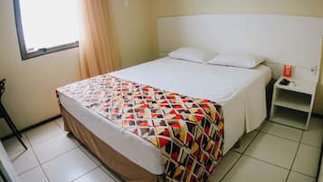A hotel room with a bed, a nightstand, a window with curtains, and an air conditioning unit.