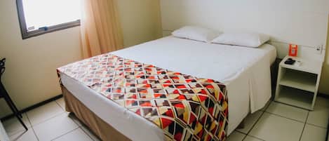 A hotel room with a bed, a nightstand, a window with curtains, and an air conditioning unit.