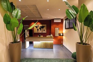 A reception area with a wooden reception desk, a world map on the wall, and large potted plants. - Kleopatra Design Hotel (Naples)