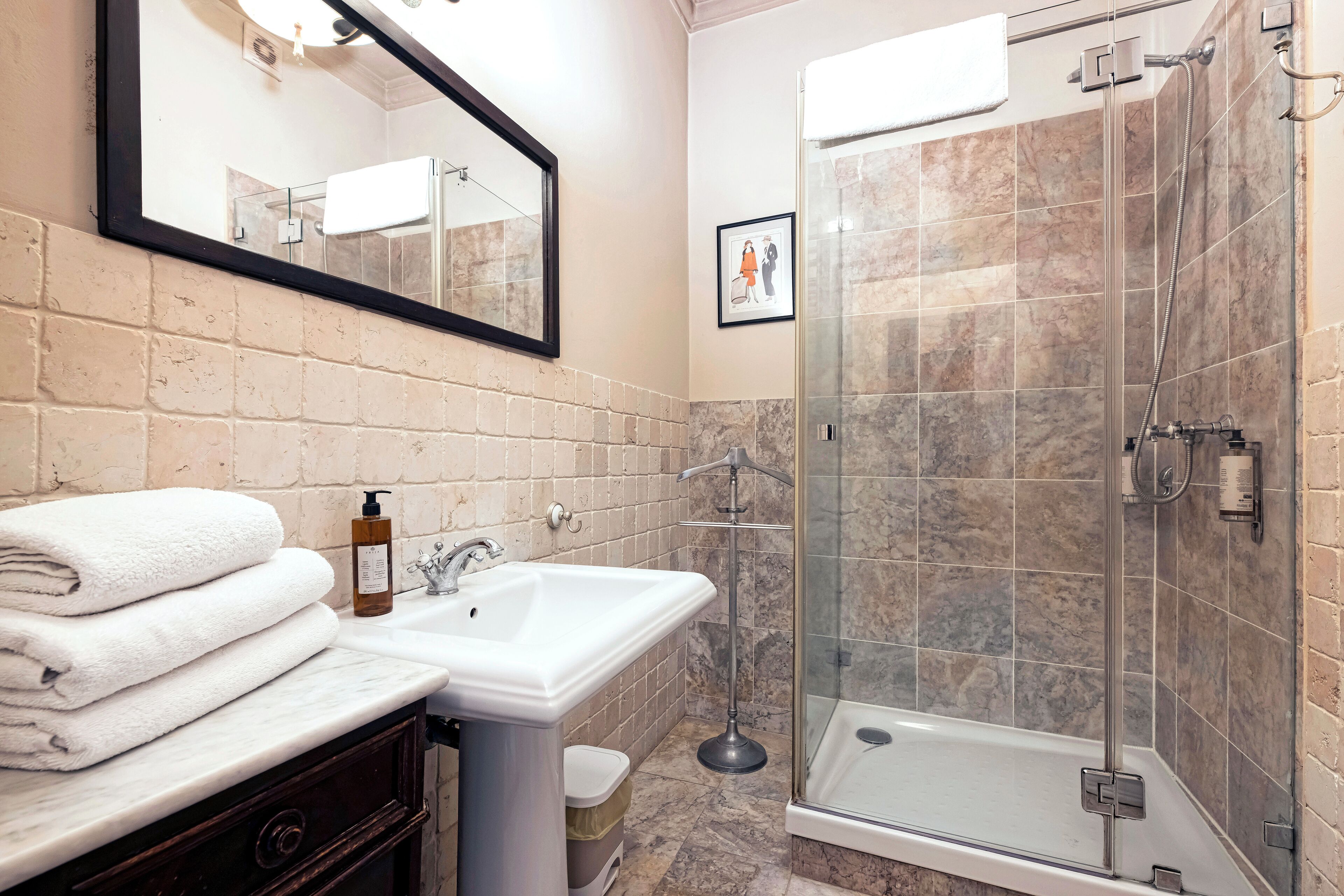 A bathroom with a marble sink, a glass shower enclosure, and a mirror above the sink.