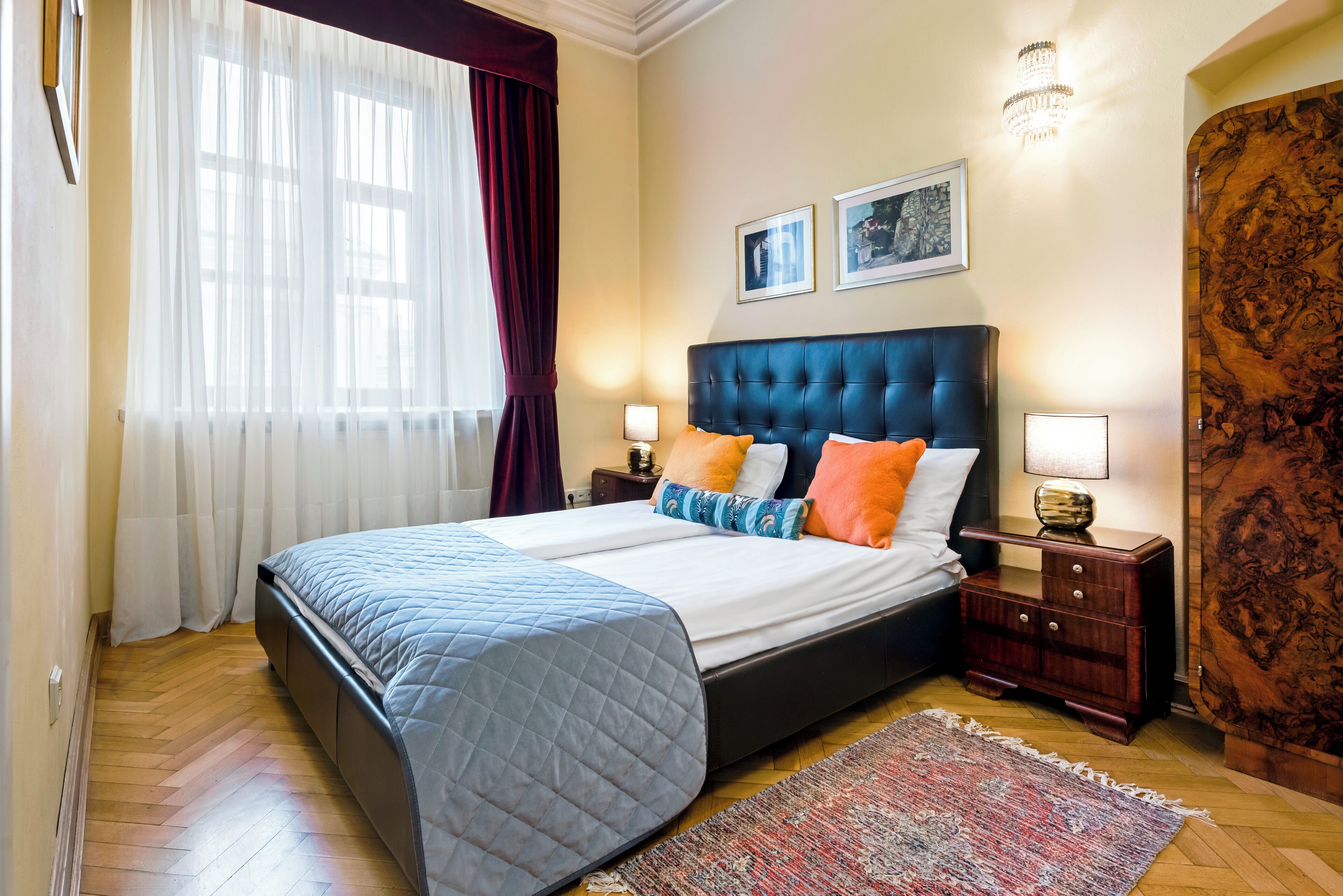 A bedroom with a large bed, two bedside tables, a nightstand, a rug, and a window with curtains.