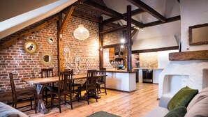 Een gezellige loft-achtige woonruimte met zichtbare houten balken, een bakstenen muur en een eethoek met houten meubels.