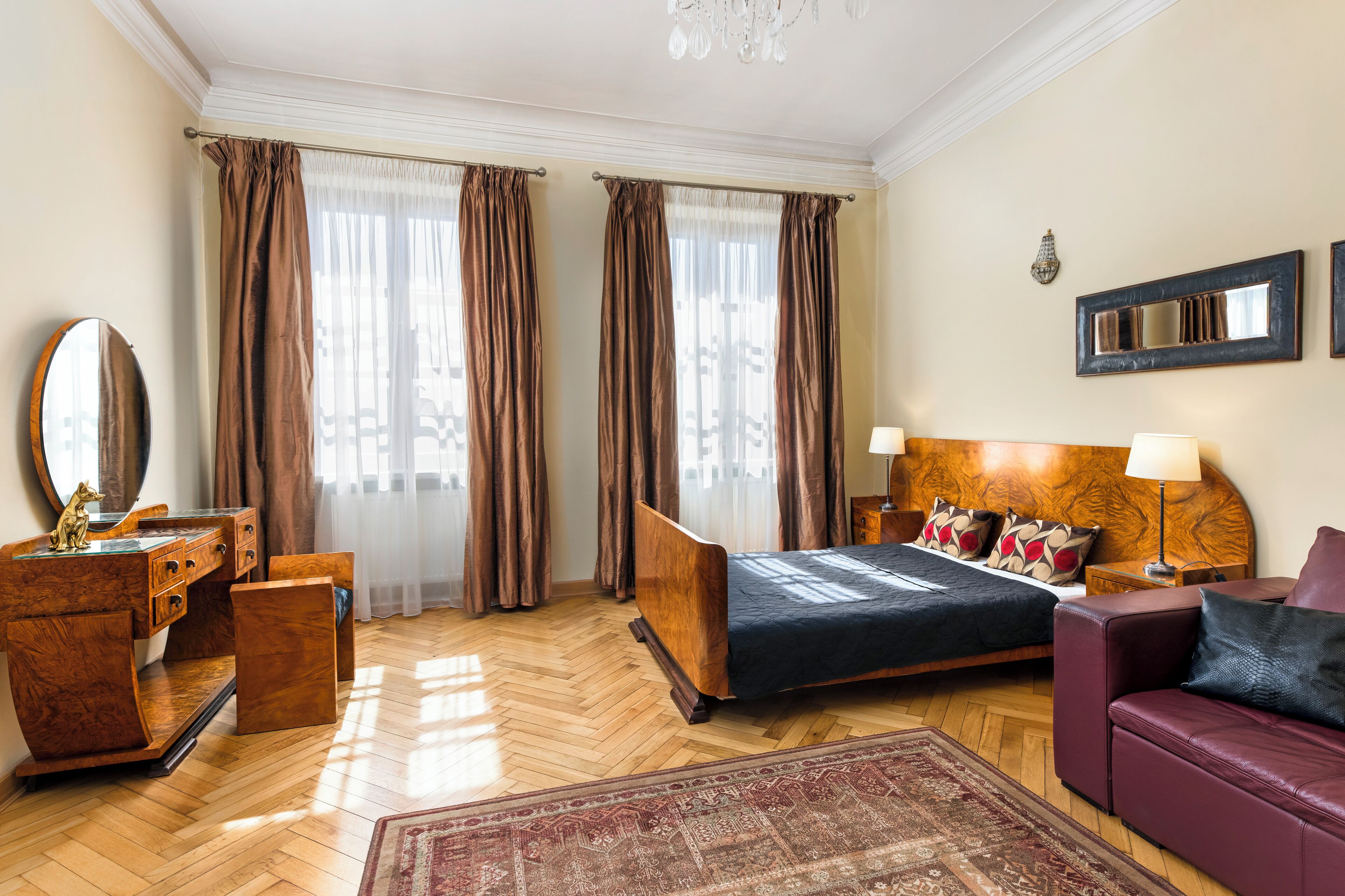 A hotel room with a wooden bed, a wooden dresser, a mirror, a wooden nightstand, a red sofa, and a patterned rug.