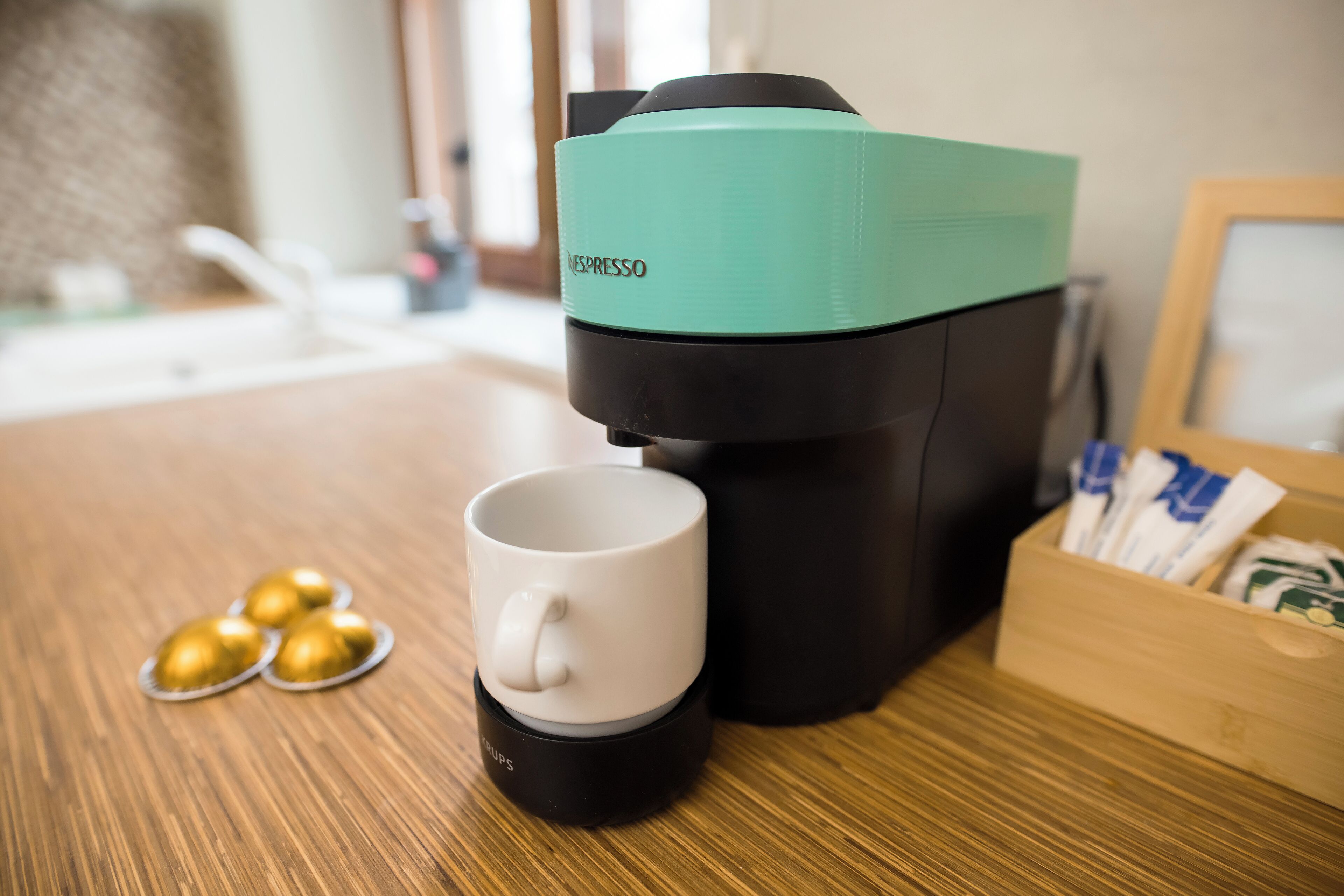 Une machine à café Nespresso avec une tasse blanche et des capsules, posée sur une table en bois.