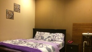 Une chambre à coucher comprenant un lit, une table de chevet et un téléphone fixé au mur, ainsi qu’une salle de bain avec un lavabo.