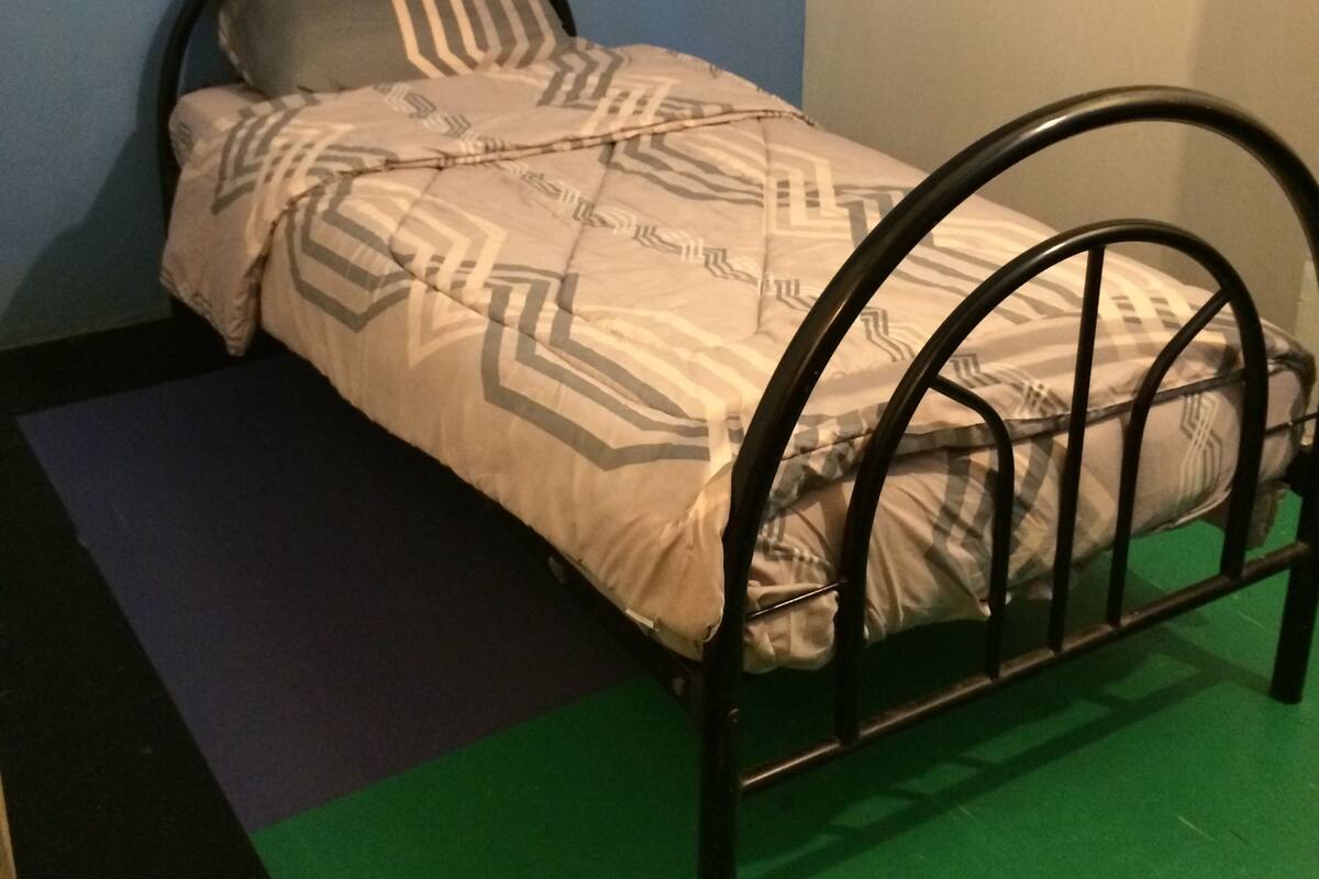 A small bed with a metal frame, a patterned bedspread, and pillows against a blue and white wall.