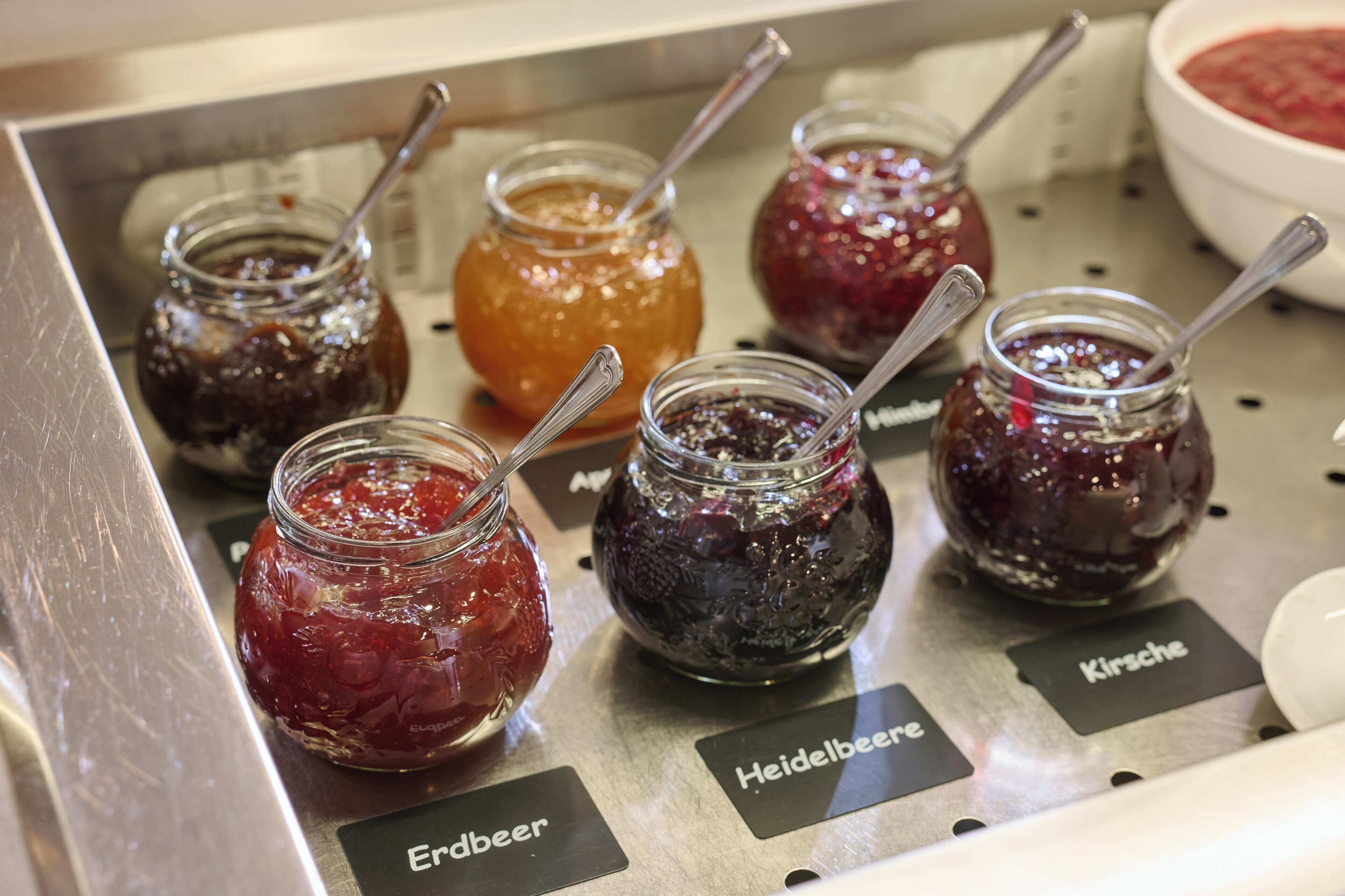 A display of various jams with labels indicating names like 'Erdbier' and 'Heidelbeer.'