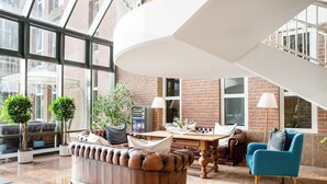 A spacious lobby with a leather sofa, a blue armchair, and a wooden table. - Stadthotel Eckernförde (Eckernfoerde)