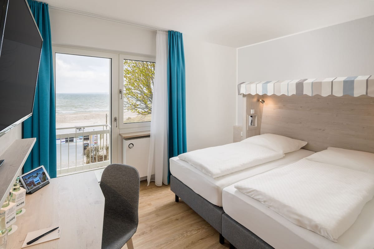 A hotel room with a bed, a desk with a computer, and a view of the beach.