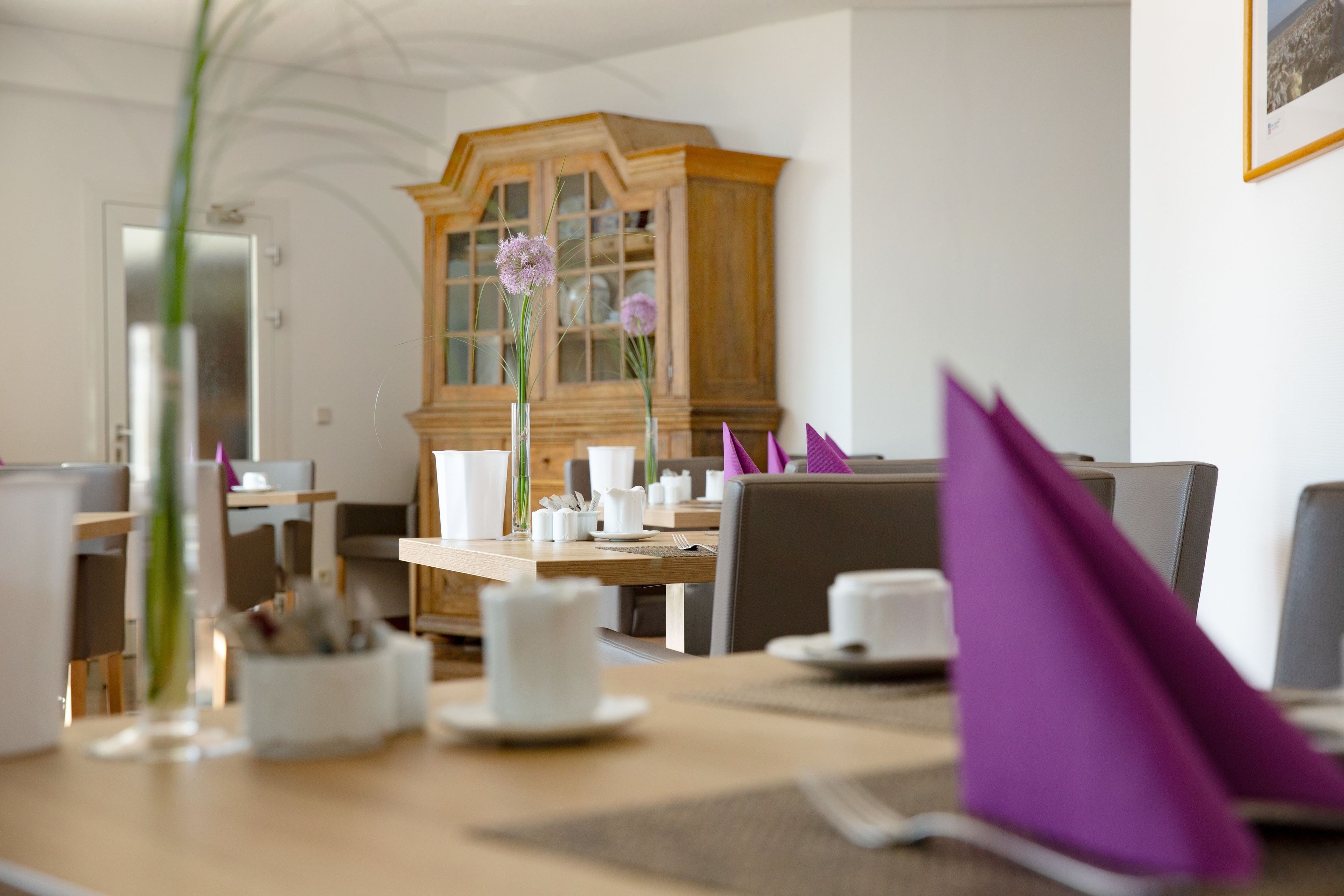 A dining area with a wooden cabinet, white tableware, and purple napkins.