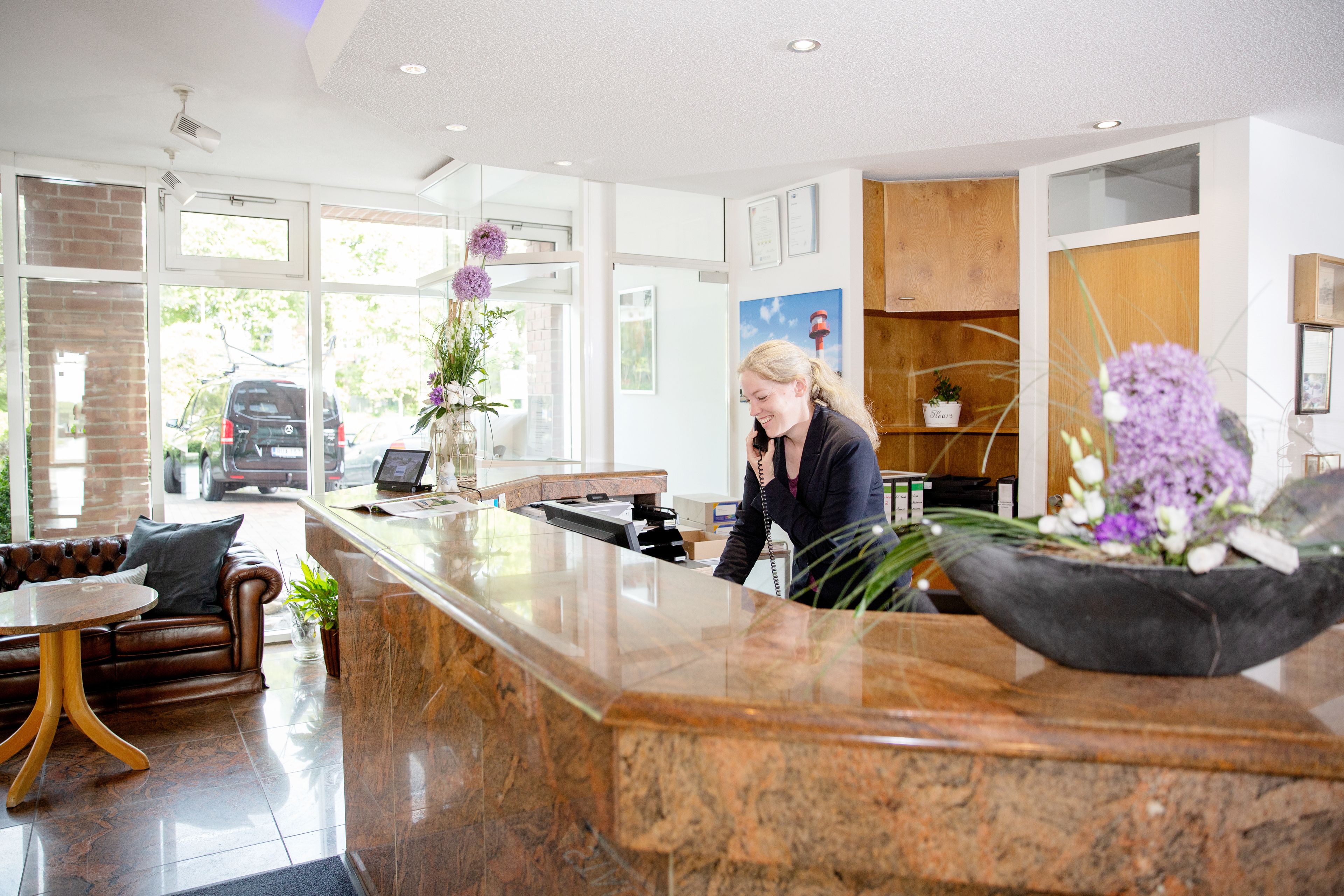 A reception area with a marble counter, leather sofa, and a large window with a view of parked cars.