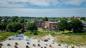 A residential area with a large brick building, a sandy beach with numbered beach huts, and a clear sky. - Stadthotel Eckernförde (Eckernfoerde)