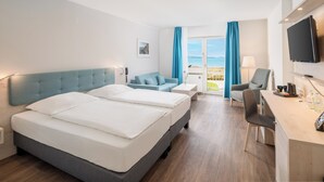 A hotel room with two beds, a desk, a chair, a TV, and a view of the sea. - Stadthotel Eckernförde (Eckernfoerde)