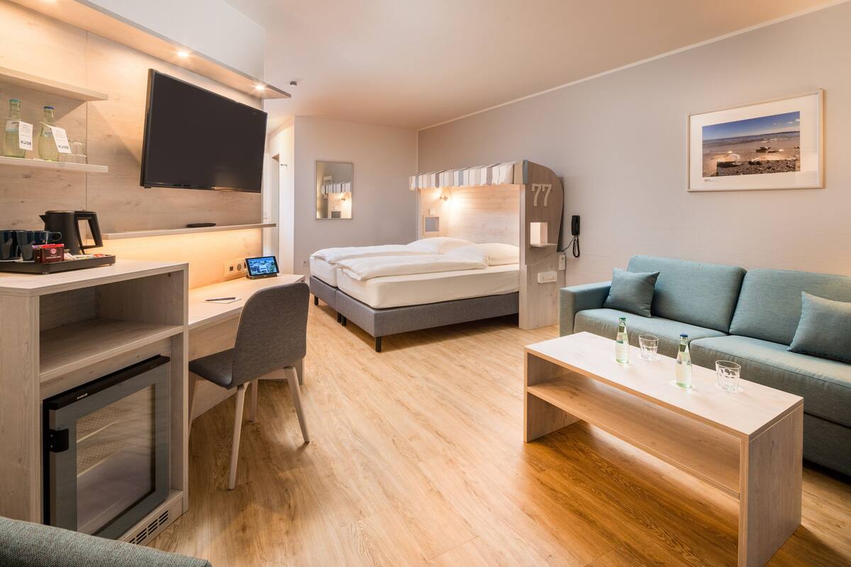 A modern hotel room with a bed, a desk, a TV, a sofa, and a coffee table.